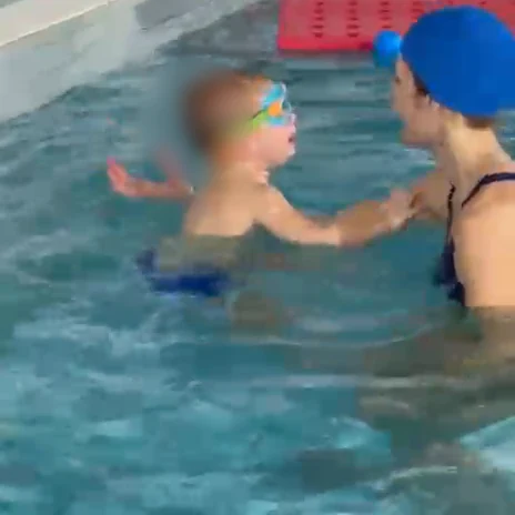 Un bambino con gli occhialini nuota da solo verso le braccia dell'istruttrice